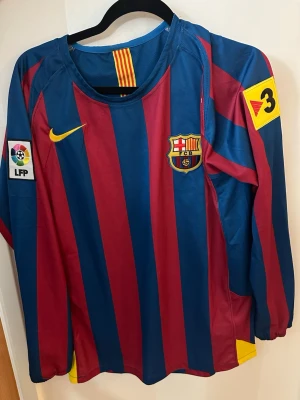 FC Barcelona långärmad Ronaldinho tröja - Säljer en långärmad FC Barcelona matchtröja från Nike med blå och vinröda ränder, klubbmärke på bröstet och Ronaldinho 10 tryckt på ryggen. Tröjan har gula detaljer och officiella La Liga och TV3-patchar på ärmarna. Perfekt för dig som älskar fotboll och Barca. Size s pris kan diskuteras 