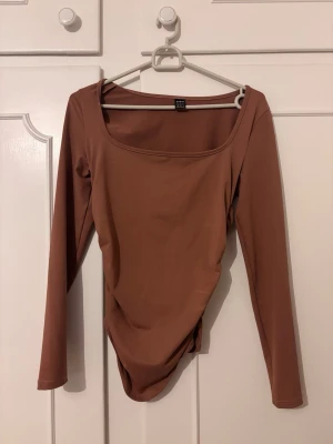 Brun långärmad body  - Snygg brun body med långa ärmar och fyrkantig ringning från Shein. Tillverkad i ett stretchigt och mjukt material som sitter skönt mot kroppen. Perfekt att styla med jeans eller kjol för en trendig look.