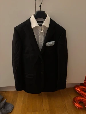 Svart kostym med vit skjorta - Säljer en klassisk svart kostym från dressman  som inhåller (kostym,skjorta,fin byxor,näsduk,galge och skyddsplast) storlek är skjortan=x long slim fit kavajen= 48 long byxorna= 31/34 