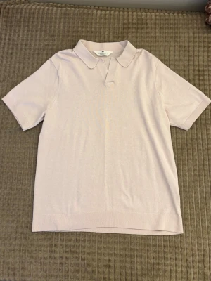 Ljusrosa stickad polotopp från H&M - Säljer en ljusrosa stickad polotopp med korta ärmar och klassisk krage. Toppen har en mjuk och bekväm känsla, perfekt för en clean och stilren look. Ribbad kant nedtill och vid ärmsluten för extra detalj.