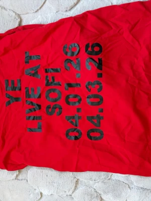 Ye live at sofi merch - Röd långärmad t-shirt i bomull från YE med stora svarta stjärnor på framsidan och ärmarna. Baksidan har svart tryck med texten 'YE LIVE AT SOFI' och datum. Perfekt för dig som gillar unika statement-plagg och streetwear.