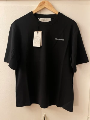 Svart t-shirt från Golden Goose - Snygg svart t-shirt från Golden Goose med minimalistisk vit logotyp på bröstet. Klassisk rund halsringning och korta ärmar. Tillverkad i mjuk bomull för en skön känsla. Perfekt för dig som gillar stilrena och trendiga plagg.