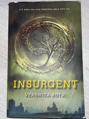 Insurgent av Veronica Roth - Insurgent är andra delen i Veronica Roths dystopiska trilogi. Omslaget är grönt med ett träd i en cirkel och tydlig gul titel. Boken är på svenska och riktar sig till unga vuxna som gillar spännande science fiction och fantasy.