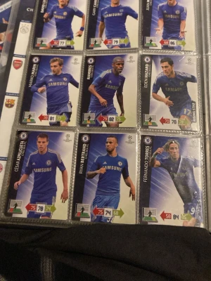 Chelsea fotbollssamlarkort från 2012/2013 - Samling med Chelsea FC fotbollssamlarkort från Champions League, snyggt organiserade i plastficka. Korten har blå och vita färger, klubbens logga och spelarnas namn. Perfekt för dig som gillar fotboll och samlarprylar.