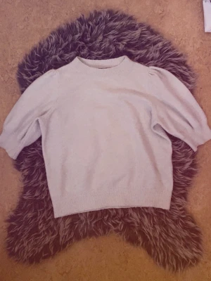 Ljusbeige/vit stickad tröja puffärm -  ljusbeige/vit stickad tröja med puffärmar och rund hals. Tröjan har ribbade muddar vid ärmslut och nederkant, och är i en mjuk och skön kvalitet.