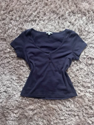 topp med knappar från Subdued - Säljer en svart topp från Subdued med korta ärmar och u-ringning. Toppen har två små knappar framtill och är i mjukt bomullsmaterial. Perfekt till jeans eller kjol för en enkel och snygg look. Använd 1 gång🤍