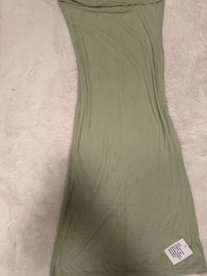 Ljusgrön axelbandslös långklänning - Snygg ljusgrön långklänning med axelbandslös design. Klänningen har en smickrande, figurnära passform och är tillverkad i ett mjukt och stretchigt material som känns bekvämt mot huden. Perfekt för dig som vill ha en stilren och enkel look.