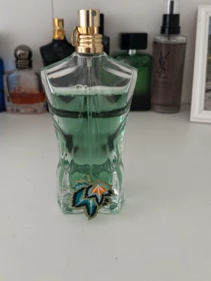 Jean Paul paradise garden  - Ikonisk parfymflaska formad som en manlig torso, fylld med grön vätska och dekorerad med ett färgglatt lövmotiv. Flaskan har en guldfärgad spraykork och är tillverkad i genomskinligt glas. Perfekt för dig som gillar unika och snygga designer. Org förpackning finns ej kvar