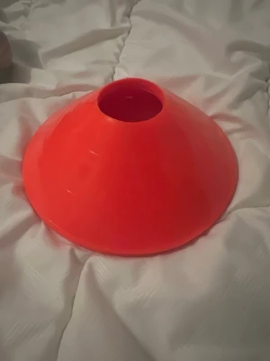 Orange träningskon för sport - Säljer flera orange träningskon i plast, perfekt för att markera banor eller övningar på fotbollsplanen eller under andra sportaktiviteter. Konerna har en rund form med hål i mitten och är lätt att bära med sig. Passar för både utomhus och inomhus träning.