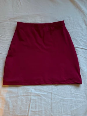 Mörkröd kortkjol i bomull - En enkel och stilren mörkröd kortkjol med rak passform och resår i midjan. Kjolen är gjord i mjukt bomullstyg och passar perfekt till både vardagsoutfits och mer uppklädda looks.