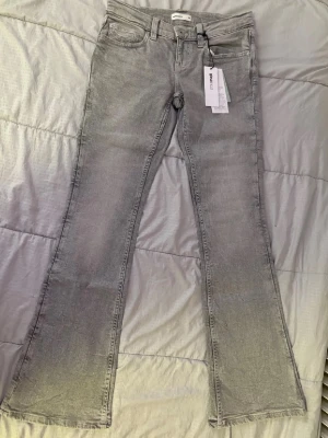 Grå bootcut jeans från Gina Tricot - Säljer ett par snygga grå bootcut jeans från Gina Tricot. Jeansen har klassisk femficksmodell, hällor för skärp och en lätt utsvängd passform nedtill. Materialet är mjukt denim med en tvättad look. Perfekta för dig som gillar trendiga silhuetter. Ultra low rise bootcut jeans