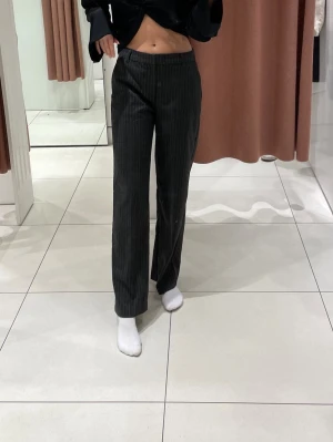 Randiga kostymbyxor  - Säljer ett par gråa kostymbyxor med tunna vita ränder från Gina tricot. Byxorna har rak passform,  låg/mellan midja, framfickor och hällor för skärp. Materialet är mjukt. Säljs pga att de är lite förkorta för mig som är 170 cm lång💕endast använda ett fåtal gånger