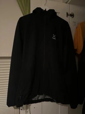 Svart vindjacka från Haglöfs - Snygg svart vindjacka från Haglöfs med minimalistisk design och vit logga på bröstet. Använd fåtal gånger. Inga täcken på användning. Skriv för fler bilder och pris kan såklart diskuteras! 