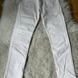 Guess jeans storlek  30 - Ett par vit rosa jeans från Guess Jeans, modell Beverly Slim Fit. Byxorna har dragkedja och knappstängning framtill samt fickor både fram och bak. Bensluten har dekorativa dragkedjor.