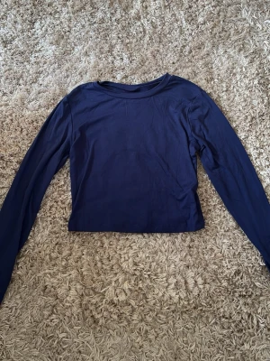 Mörkblå croppad långärmad topp - En enkel och stilren mörkblå croppad topp med långa ärmar. Perfekt att matcha med höga jeans eller kjol för en clean look. Tillverkad i mjukt material som känns skönt mot huden.
