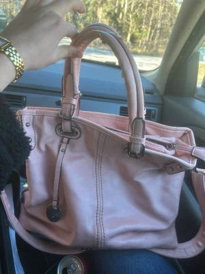 Ljusrosa handväska med silverdetaljer - Snygg ljusrosa handväska med dubbla handtag och silverfärgade metalldetaljer.  Stor snygg rosa väska. Ganska sliten