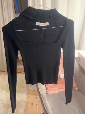 Svart ribbad topp från Bershka - Trendig svart ribbad topp från Bershka med lång ärm och fyrkantig urringning. Toppen har en croppad passform och är tillverkad i stretchigt material som sitter snyggt på kroppen. Perfekt att styla med höga jeans eller kjol.