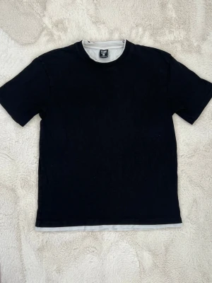 Svart basic t-shirt  - En svart basic t-shirt. Tillverkad i mjuk bomull. T-shirten har en enkel och clean look med en liten kontrastkant i vitt längst ner.