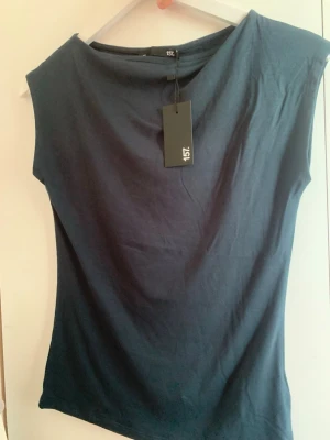 Mörkblå ärmlös topp från 157 - Snygg mörkblå topp från 157 i ärmlös modell. Toppen har en enkel, rak passform och är tillverkad i mjuk bomull som känns skön mot huden. Perfekt att matcha med jeans eller kjol för en clean look. Bra för sommaren!! HELT NY MED PRISLAPP KVAR!!!!