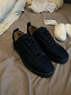Mörkblå sneakers från Christian Louboutin - Snygga mörkblå sneakers från Christian Louboutin med klassisk röd sula och diskret logga. Skorna har ovandel i mocka, svarta skosnören och låg profil. Perfekta för dig som vill ha en stilren och exklusiv look.