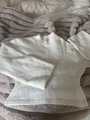 Vit stickad tröja Gina Tricot - Säljer en enkel och stilren vit stickad tröja från Gina Tricot i storlek XS. Tröjan har rund halsringning, långa ärmar och ribbade muddar vid hals, ärmslut och nederkant. Perfekt basplagg till garderoben! Tröjan är från gina 14+ och har en liten defekt, ett håll vid axeln men inget som syns stort. Hållet var där när jag köpte den🥰