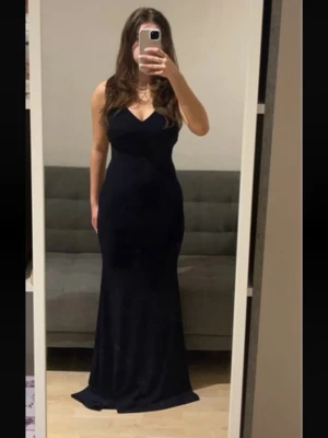Mörk marinblå långklänning med öppen rygg - Elegant mörk marinblå långklänning med smala axelband som korsas i ryggen och en djup v-ringning framtill. Klänningen har figurnära passform, den är stretchig och en stilren, tidlös design som passar perfekt till speciella tillfällen. Den är även oanvänd.