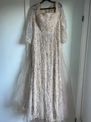 Lång glittrig klänning med paljetter - Elegant långklänning i champagnefärg med transparenta långärmar och täckt av glittriga paljetter i ett mönster över hela klänningen. Klänningen har en lätt utsvängd kjol och ger en lyxig känsla, Aldrig använt, ny. Beställdes från en butik i Turkiet. Säljer pga den var för liten! Det står storlek 14 men den passar M-L. Sitter jätte fint på! Man kan även ta bort det extra tyget där bak! Då blir det ännu snyggare. Har inbyggd BH i! (Den kom utan prislapp men den är helt ny som sagt! Ord pris 6000kr