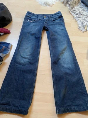 Mörkblå bootcut jeans från Replay - Säljer ett par mörkblå bootcut jeans från Replay med klassisk femficksmodell och snygga slitningar framtill. Jeansen har låg midja, gylf med dragkedja och knapp samt detaljerade sömmar. Perfekta för en avslappnad och trendig look. De vita trådarna är från när jag försökte göra de ännu mer lådmidjade men det blev konstigt så fick sprätta upp! De var för långa för mig därav blev lite slitna där nere