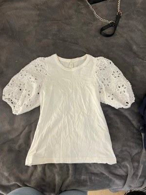 Vit T-shirt  - En gullig T-shirt som är perfekt för våren / sommaren, men kan såklart användas året om. Fina ”volang” mönster på armarna. Endast använd ett få tal gånger. Pösiga armar som sitter åt längst ner med mycket stretch. 