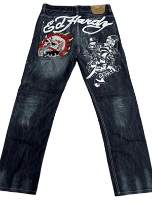 Vintage Rare Y2K Ed Hardy Printed Embroidered Logo Skull Jeans - Det är med sorg jag måste sälja de finaste jeansen jag äger då de tyvärr inte kommer till användning, och sitter snarare som en dekoration i mitt rum. De är verkligen superfina! Kolla gärna bilderna noggrant, tråden på vissa ställen har tappat lite av sin färg men det är verkligen inget man tänker på!    Skriv vid frågor eller om du vill diskutera pris!   Storlek L (se bild)   Measurements: 90cm/ 35,4” in top od the jeans  110cm/ 43,3” length