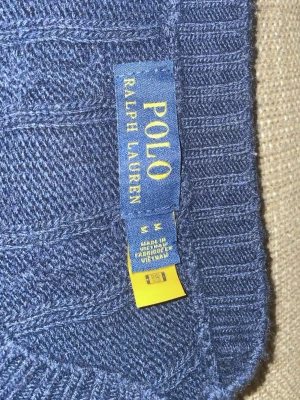 Marinblå kabelstickad tröja Polo Ralph Lauren - Säljer en marinblå kabelstickad tröja från Polo Ralph Lauren. Tröjan har rund hals, långa ärmar och klassisk röd broderad logga på bröstet. Ribbstickade muddar vid ärmslut och nederkant. Perfekt för en stilren och tidlös look.