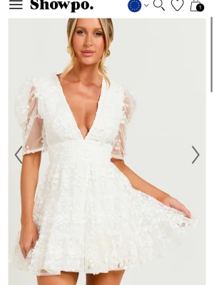 Vit kort klänning med spetsdetaljer - Supersöt vit kort klänning från Showpo med v-ringning, puffiga ärmar i transparent tyg och blommiga spetsdetaljer över hela klänningen. Den är helt oanvänd och har prislappen kvar, den är även slutsåld på hemsidan! Perfekt till studenten🥰 