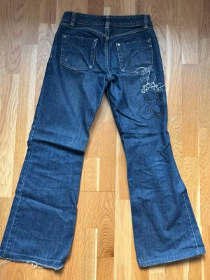 Blå bootcut jeans med brodyr - Säljer ett par blå bootcut jeans från Replay med snygg brodyrdetalj på ena bakfickan. Jeansen har fem fickor, låg midja och råa, fransiga benslut. Klassisk denimlook med slitningar och kontrastsömmar💕💕 midjemått: 36/37 cm innerbenslängd: 73cm