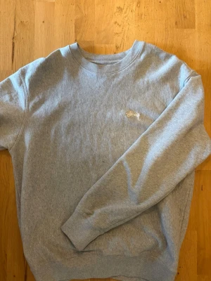 Grå sweatshirt från Stüssy - Klassisk grå sweatshirt från Stüssy med broderad logga i vitt på bröstet. Bra skick, strl M men stussy har ganska stor passform så funkar även som L