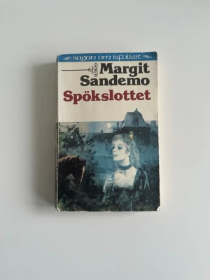 Bok ”Spökslottet” av Margit Sandemo - Säljer boken 'Spökslottet' av Margit Sandemo, del av serien Sagan om Isfolket. Omslaget har mystiska illustrationer i blå, gröna och bruna toner med en spöklik stämning. Perfekt för dig som gillar övernaturliga romaner och nordisk fantasy.