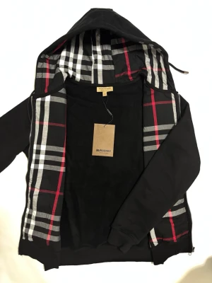 Burberry zip hoodie - Stilren Burburry kofta med broderat logga på bröstet. Perfekt för dessa kyliga dagar och kväller. Storleken är M men kan även passa någon med ett större S. Skickas imon 24 timmar!