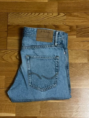 Blå Jack & Jones jeans - Klassiska blå jeans från Jack & Jones Jeans med rak passform och fem fickor. Jeansen har en ljus tvätt, Tillverkade i slitstark denim, perfekta för en avslappnad och trendig stil. Stl W28 L32