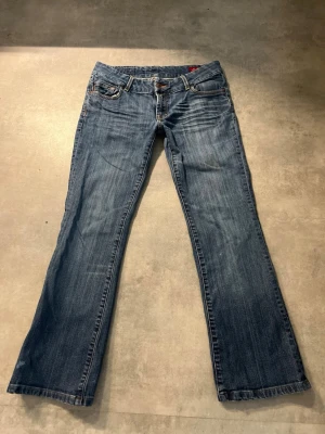 Blå bootcut jeans med låg midja - Snygga blå bootcut jeans med låg midja och klassisk femficksdesign. Jeansen har en lätt tvättad look och raka ben. Perfekta för en avslappnad och trendig stil. Passar dig som gillar en retro vibe.