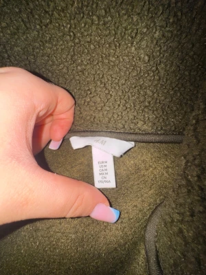 Olivgrön teddyjacka från H&M - Mysig olivgrön teddyjacka från H&M i storlek M. Jackan har en fluffig och mjuk textur som ger en riktigt chill vibe. Perfekt för att hålla värmen under kyliga dagar. Enkel att matcha med olika outfits och superbekväm att bära.