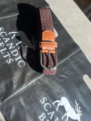 Brunt flätat bälte  - Snyggt brunt flätat bälte med detaljer i ljust brunt skinn och silverfärgat spänne. Perfekt accessoar för att lyfta din outfit och ge en stilren touch. Passar till både jeans och chinos. 105cm