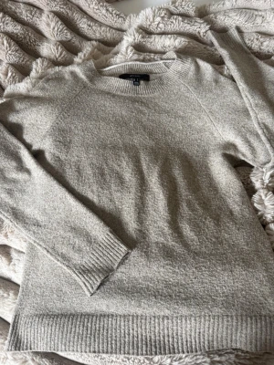 Beige stickad tröja Vero Moda - Mysig beige stickad tröja från Vero Moda med rund halsringning och ribbade muddar vid ärmslut och nederkant. Perfekt för lager på lager och enkel att matcha till olika outfits. Tillverkad i mjukt material för extra komfort.