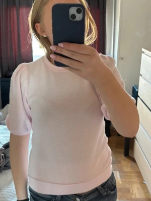 Ljusrosa topp med puffärm - Supersöt ljusrosa topp med puffärmar och rund hals. Toppen har en mjuk och stretchig känsla, perfekt för en trendig och feminin look. Passformen är normal och materialet känns som bomull eller polyester.