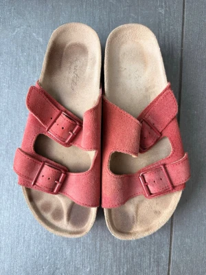 Röda platåsandaler - Säljer ett par röda sandaler från Kaotiko med två breda remmar i mocka och justerbara spännen. Sandalerna har en rejäl platåsula i kork och gummi samt en bekväm innersula. Perfekta för dig som vill ha både stil och komfort.