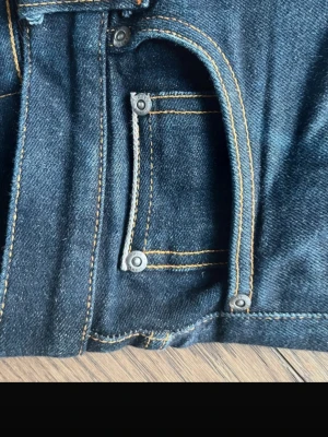 Nudie selvedge jeans - Snygga mörkblå skinny jeans från Pull&Bear med klassiska fem fickor och kontrastsömmar. Jeansen har en smal passform och är tillverkade i stretchigt denimtyg för extra komfort. Perfekta för en trendig och avslappnad look.