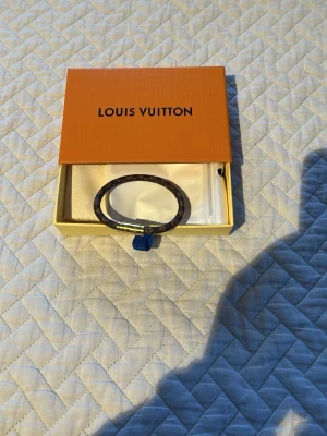 Louisss Vuittonnnnnnn brunt monogram armband - Snyggt armband från Louissss Vuittonaaa i klassiskt brunt monogrammönster med guldfärgat spänne. Armbandet har en rund form och är tillverkat i canvas med detaljer i metall. Perfekt accessoar för dig som gillar lyxiga detaljer och ikonisk design.
