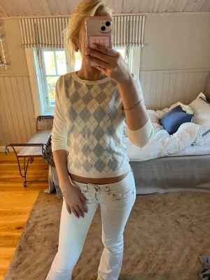 Argyle stickad tröja från Burberry - Snygg stickad tröja från Burberry i vitt med ljusblått och ljusgrönt argylemönster. Tröjan har rund halsringning, ribbade muddar och är tillverkad i mjukt material. Perfekt för en preppy look och passar till både jeans och kjol.