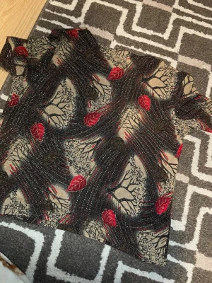 Glittrig t-shirt med röda blad - Unik t-shirt med glittrigt tyg och abstrakt mönster av röda blad och grenar. Basen är beige med inslag av svart och röda detaljer. T-shirten har korta ärmar och en rak passform med en lite lösare krage. Perfekt för dig som vill sticka ut med en cool/ lugn ellerkonstnärlig look.