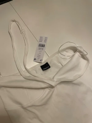 Vit ribbad topp från New Yorker - Säljer en vit ribbad topp från Gina Tricot med tunna axelband och lätt v-ringad hals. Toppen är figurnära och har en mjuk, Perfekt för att styla med jeans eller kjol för en trendig look.