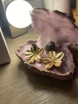 Guldiga blomörhängen i metall - Snygga örhängen i form av blommor i guldfärgad metall. De har en tydlig blomform med detaljerade blad och är perfekta för att ge din look en extra touch. Passar dig som gillar statement-smycken och vill sticka ut.