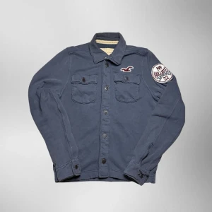 Vintage Hollister button up overshirt cardigan - herr strl M - Säljer en vintage Hollister button up overshirt cardigan i grå färg i storlek M med broderad Hollister logga på vänster sida av bröstkorgen samt på vänster ärm. Fickor upptill på varsin sida, uppfällbar krage samt knäppbara handleder  👕 Märke: Hollister 📏 Storlek: M 🎨 Färg: Grå 🧵 Material: 73% bomull, 27% polyester 📐 Mått: 70 cm lång, 55 cm bred 📌 Skick: Mycket bra skick (se bilder)  💬 Hör av dig vid frågor 💰 Pris kan diskuteras vid snabb affär 📦 Skickas inom 24 timmar